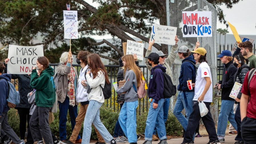 Parents and supporters protest school mask mandates in front of San Marcos High School. They hold picket signs reading "unmask our kids" and "mask choice now".