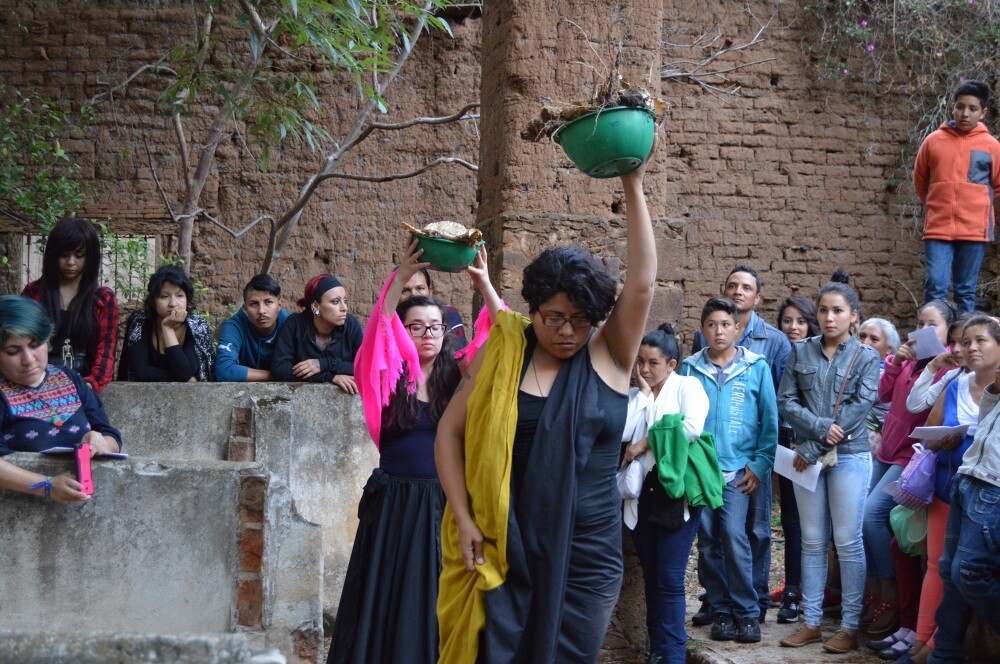 Women in black dress hold up ceramic vessels as people watch in the crowd.