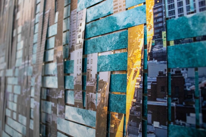 Two sheets of metal woven together. One sheet of metal has a city landscape printed on. Another sheet of metal has an ocean water landscape printed on. Then two sheets are cut in strips and are interwoven with one another.