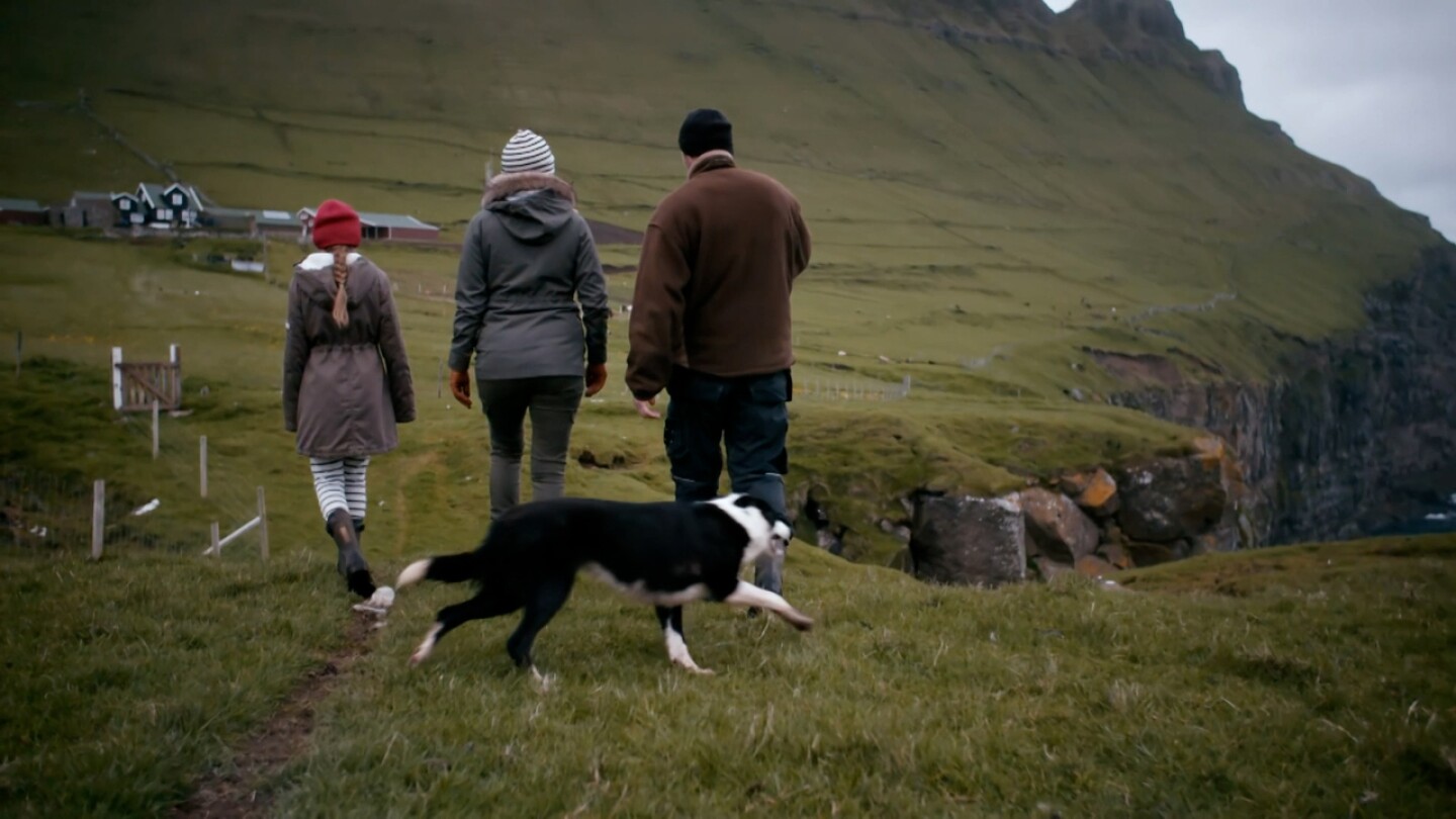 Three people and a dog walk alongside the cliffs of the Faroe Islands.