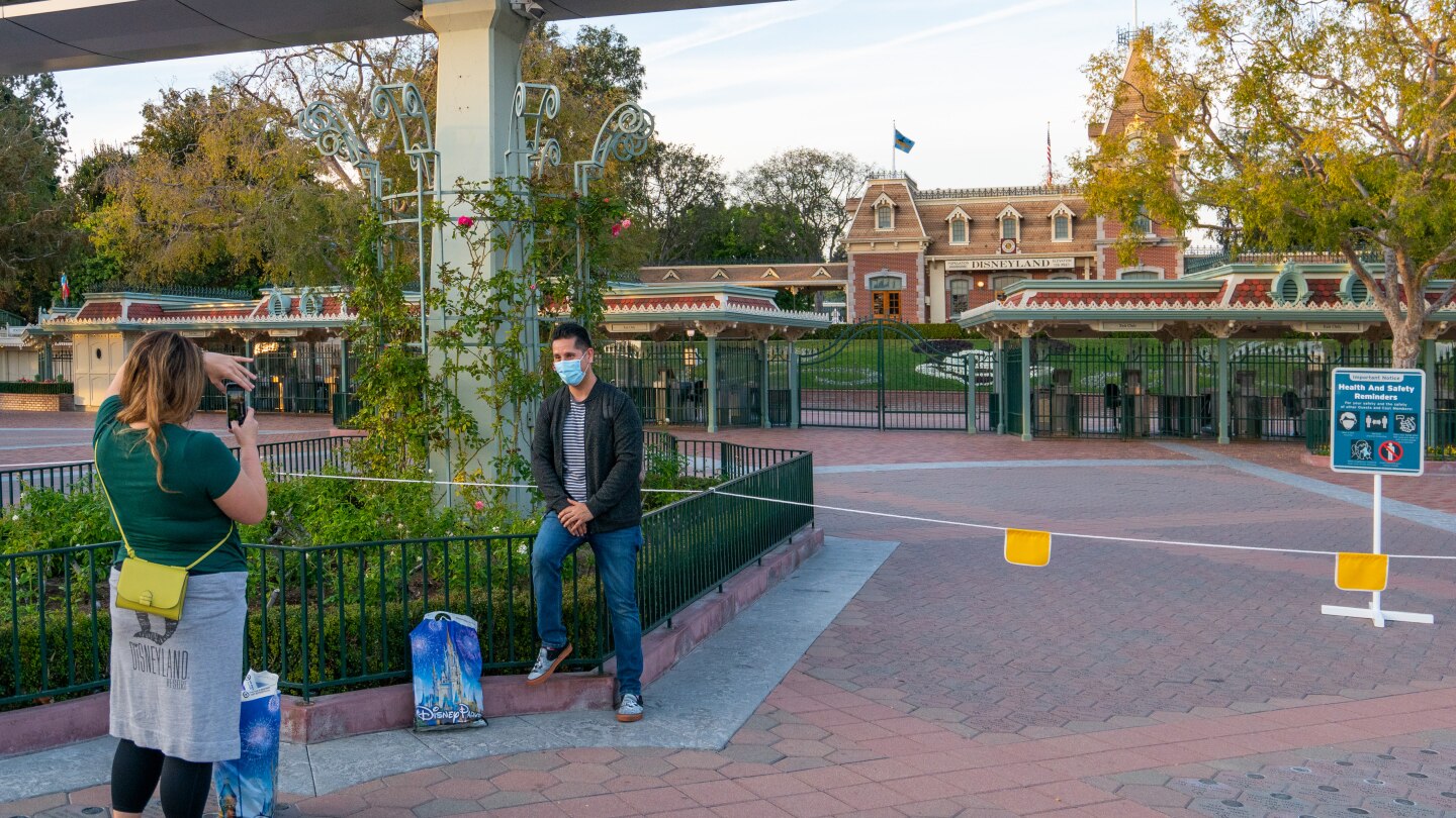 A woman takes a picture of a man outside of the closed Disneyland theme park entrance.