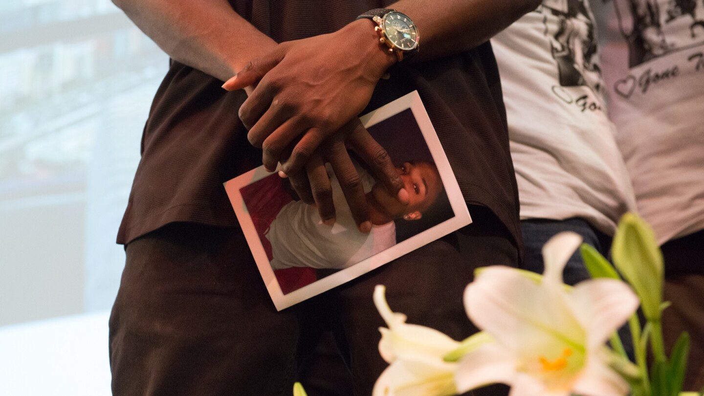 A friend of Josiah Lawson at his memorial, holding a photo of David Josiah Lawson in his hands. | Still from "Who Killed Josiah?" | Courtesy Mark McKenna