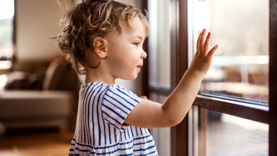 A small child looks at their reflection on a window.