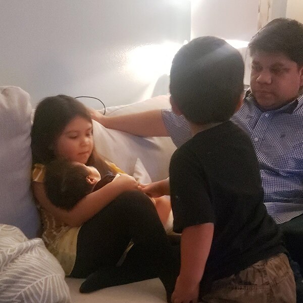 A young boy and a man watch as a little girl holds a baby.