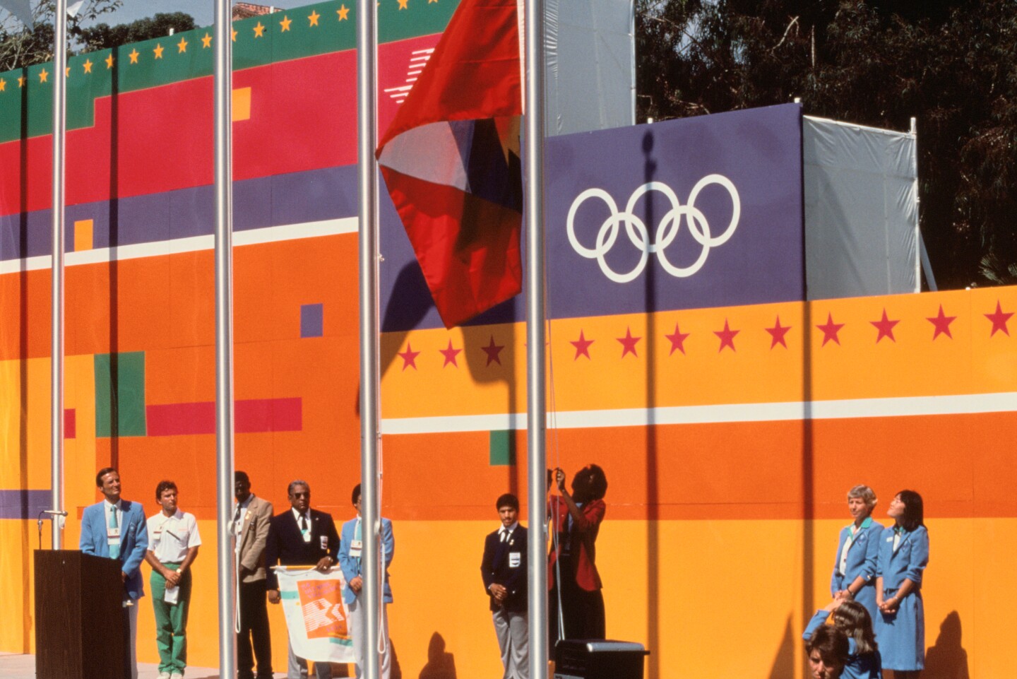 An official raises the flag during the 1984 Olympics with the bright background.