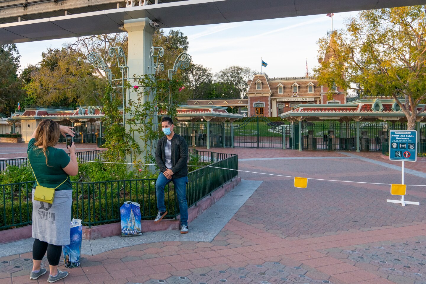 A woman takes a picture of a man outside of the closed Disneyland theme park entrance.