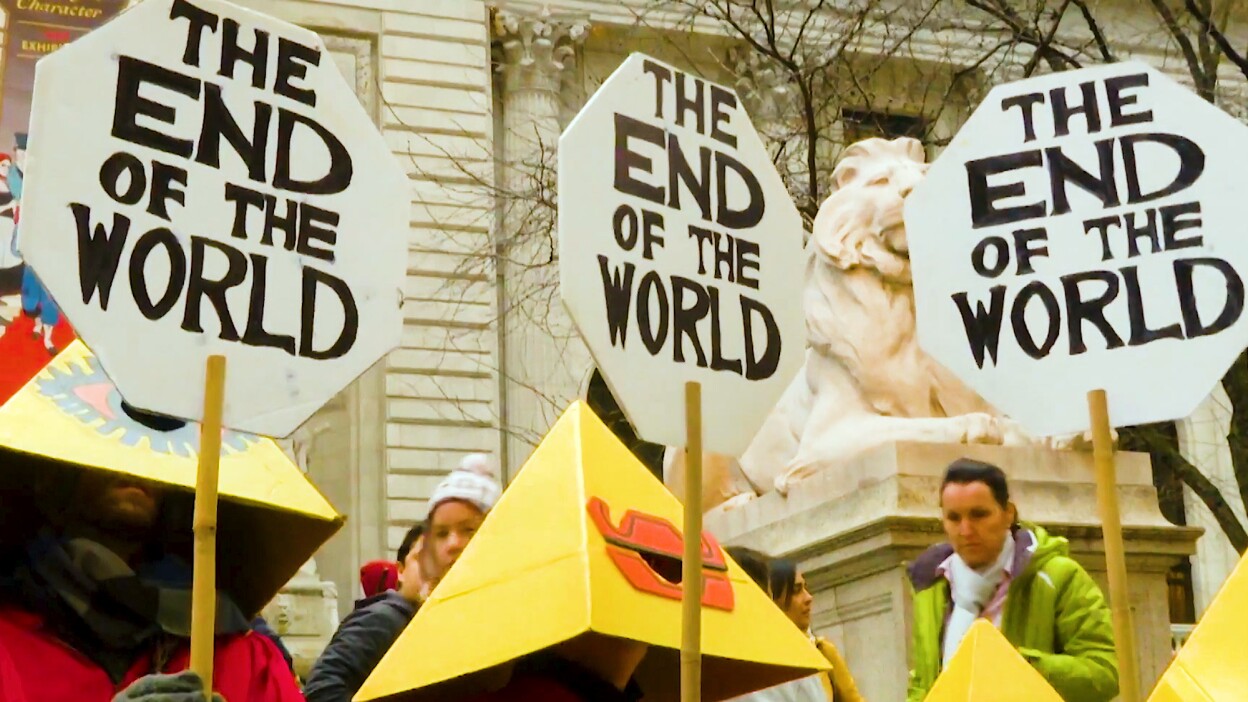 Demonstrators wearing pyramidal head coverings hold up signs that read, "The End of the World."