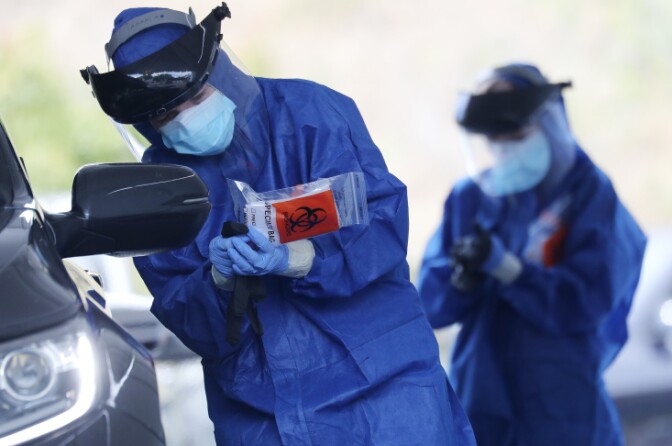 A volunteer in personal protective equipment (PPE) holds a specimen bag while conducting drive-through coronavirus testing at Malibu City Hall on April 8, 2020 in Malibu, California. | Mario Tama/Getty Images