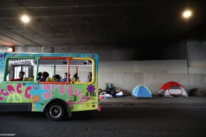 A tour bus passes a homeless encampment located beneath an overpass on June 5, 2019 in Los Angeles. | Mario Tama/Getty Images via LAist