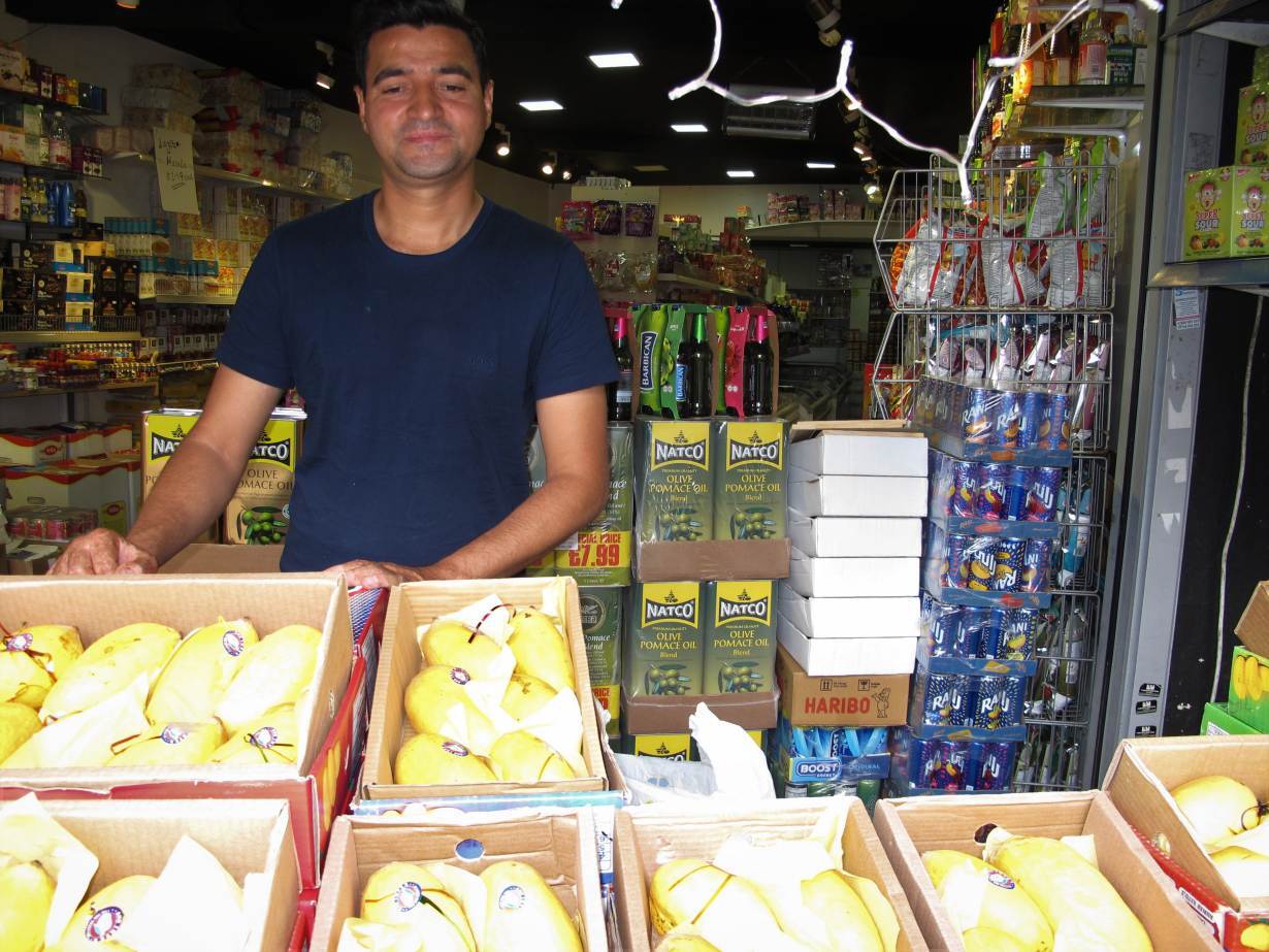 Mango vendor Asif Khaliq stands behind a display of Pakistani and Indian mangoes in the Tooting neighborhood of London, June 15, 2020. | Thomson Reuters Foundation/Laurie Goering