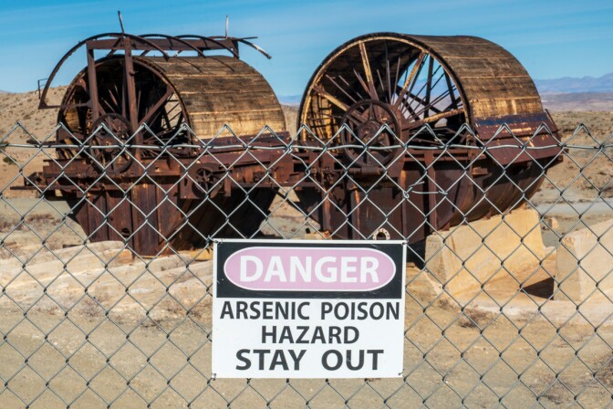 Abandoned mill machinery with an arsenic hazard warning sign shown in the foreground. | Kim Stringfellow.