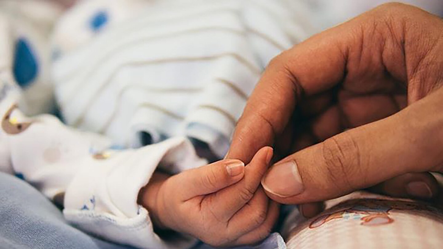 Close up of a new parent's hand holding a baby's hand.