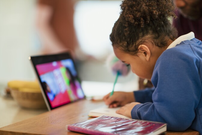 A close-up shot of a schoolgirl doing homework with the help of a digital tablet. She is at home sitting at the kitchen table.