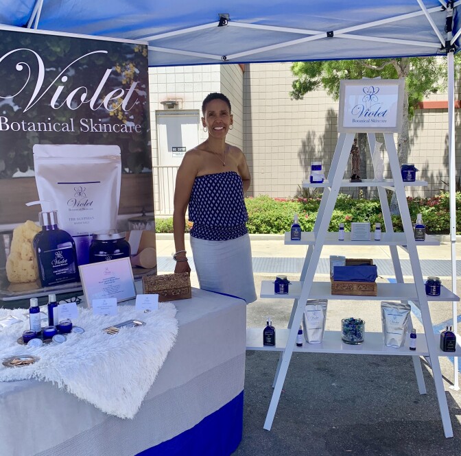 A woman stands in front of a little shop set up outdoors.
