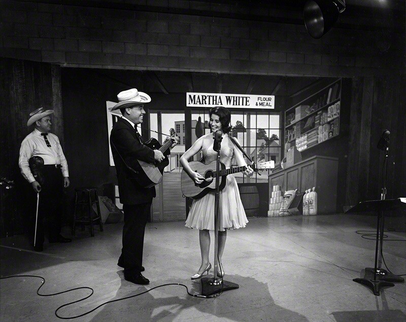 Earl Scruggs and June Carter on the set of the Flatt & Scruggs Grand Ole Opry Show, 1961. Paul Warren (in background), fiddler, Foggy Mountain Boys. © Les Leverett