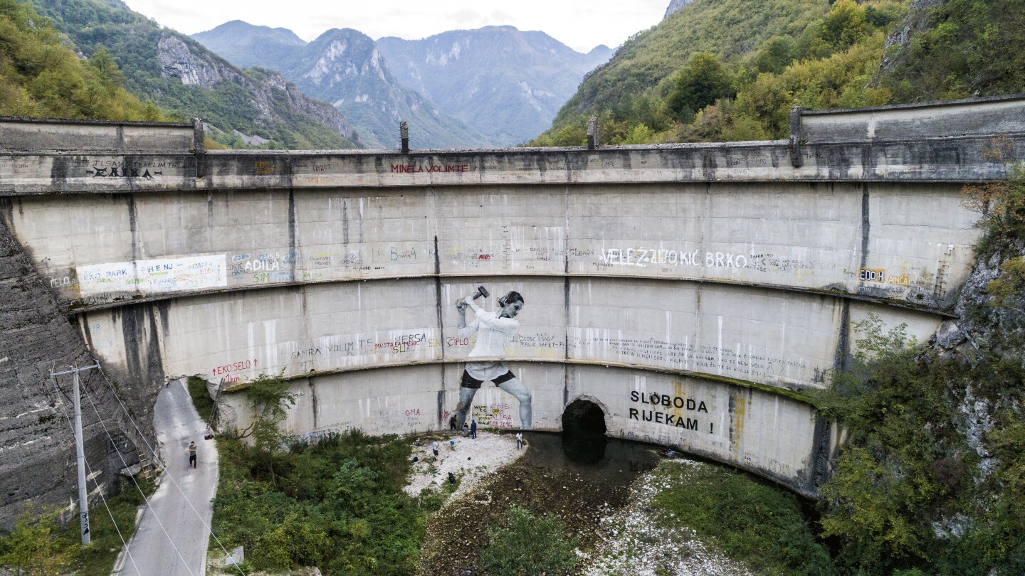 a large damn with graffiti of a woman with a hammer on it, mountains in the background