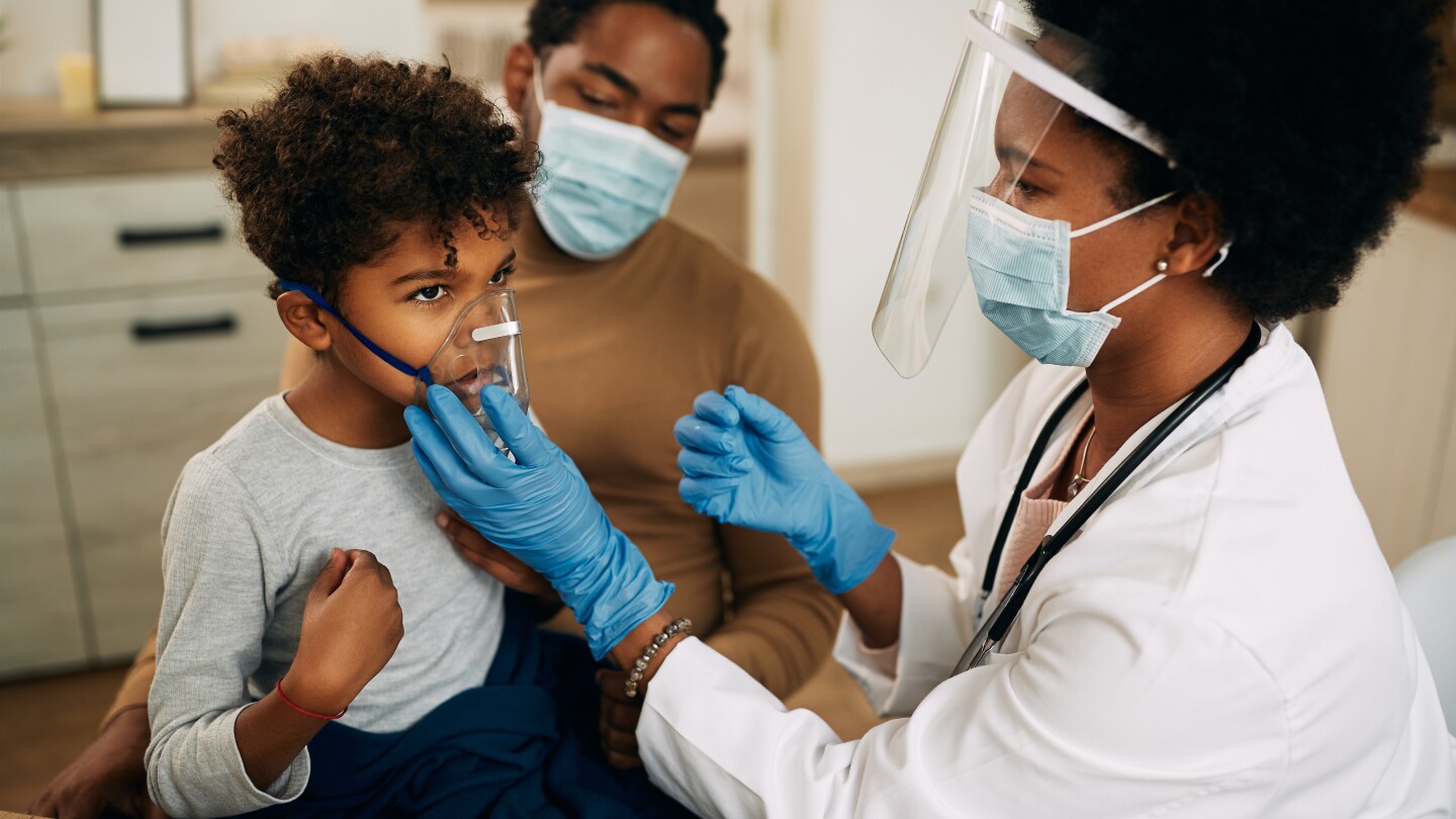 Small black boy receiving asthma treatment while doctor is vising him at home due to COVID-19 pandemic.