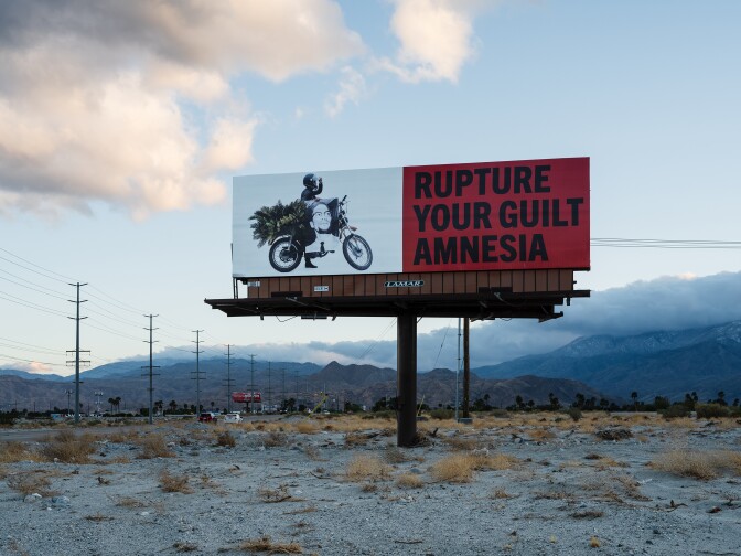 A billboard part of Simmons' art installation, "Because You Know Ultimately We Will Band a Militia," reads, "Rupture your guilt amnesia."