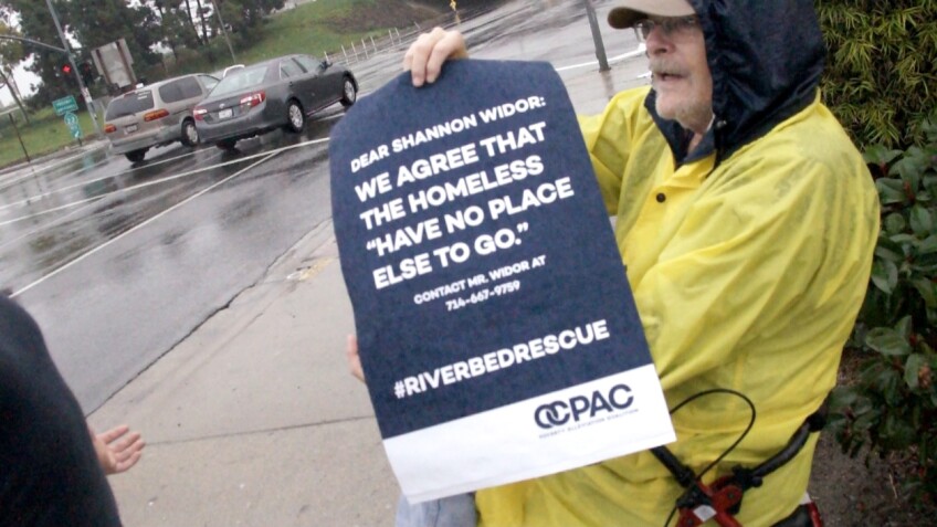 Protestor with sign addressing O.C. County Public Works Department spokesperson Shannon Widor