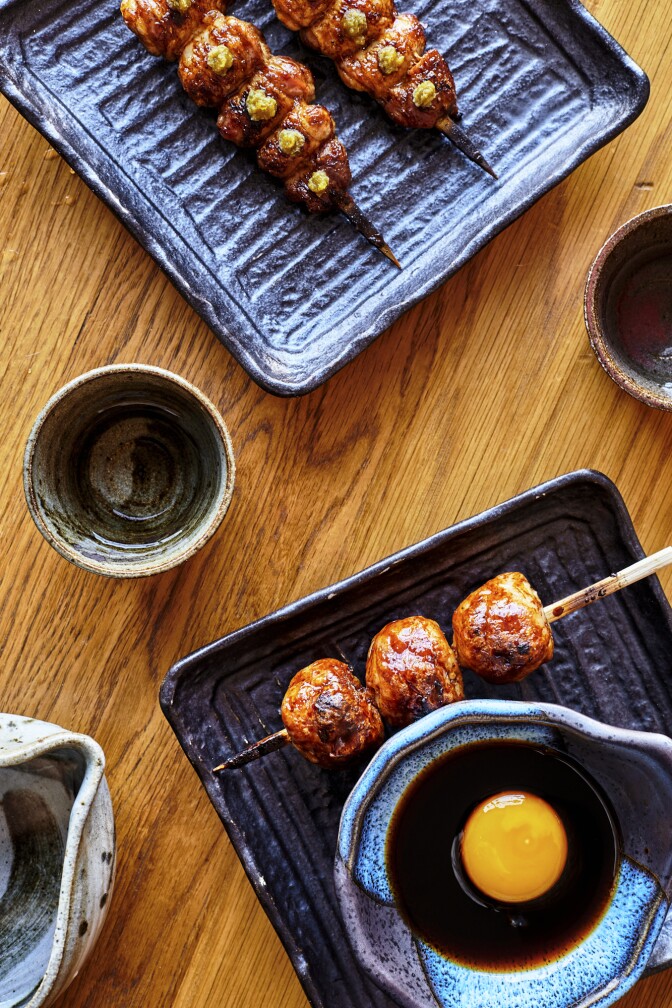 A cup of junmai sake is found set beside charcoal-grilled chicken meatballs and chicken oysters.