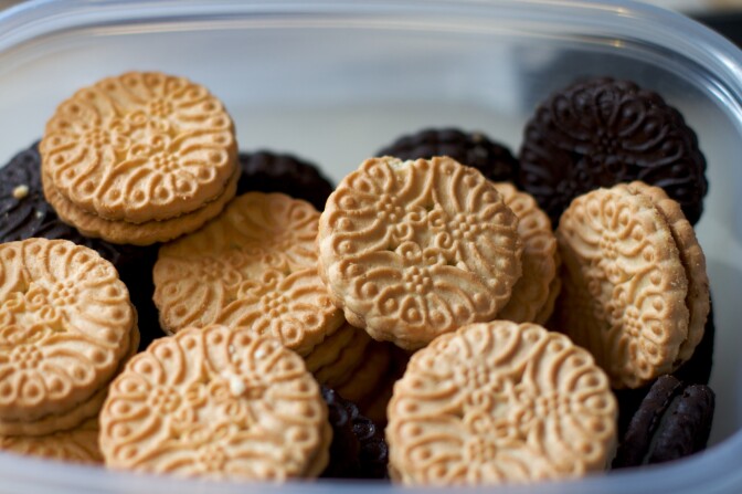 Vanilla and chocolate sandwich cookies with a swirly top sit in a small plastic container.