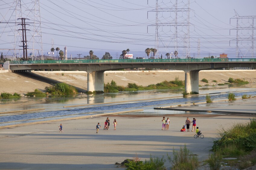 A wide shot of families walking along the concrete banks of the LA river with a bridge in the background 