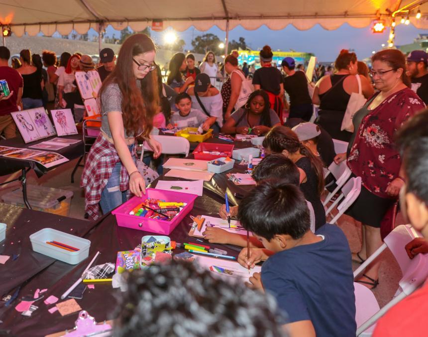 Young people make art projects while seated beside each other.