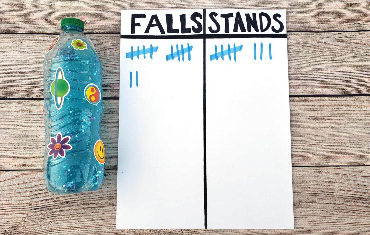 A white sheet of paper is divided into two columns labeled "falls" and "stands." There is a decorated plastic water bottle next to it.
