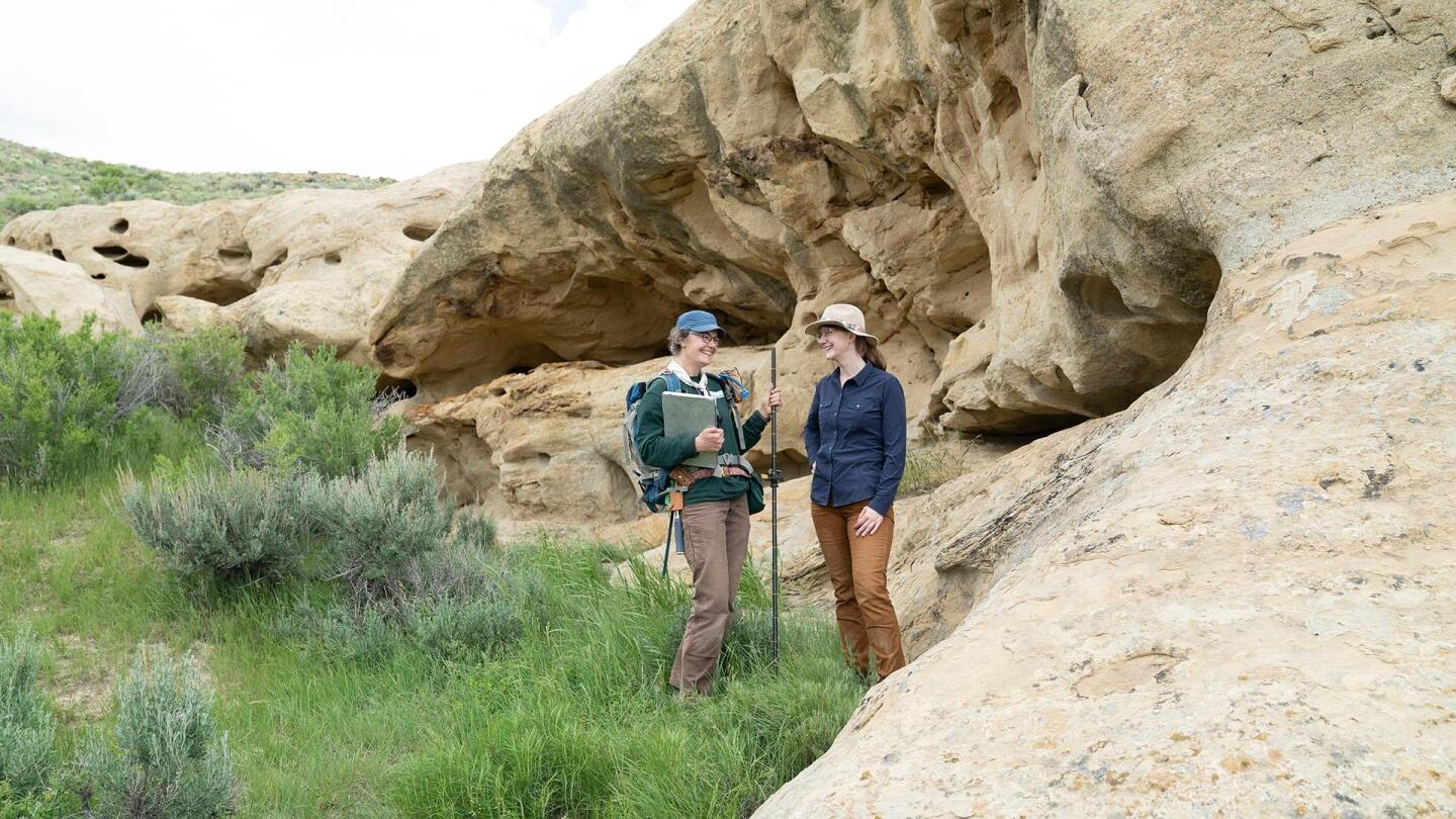 "Prehistoric Road Trip" host Emily Graslie faces another woman wearing a backpack and holding a trekking pole. | "Prehistoric Road Trip: Tiny Teeth, Fearsome Beasts"
