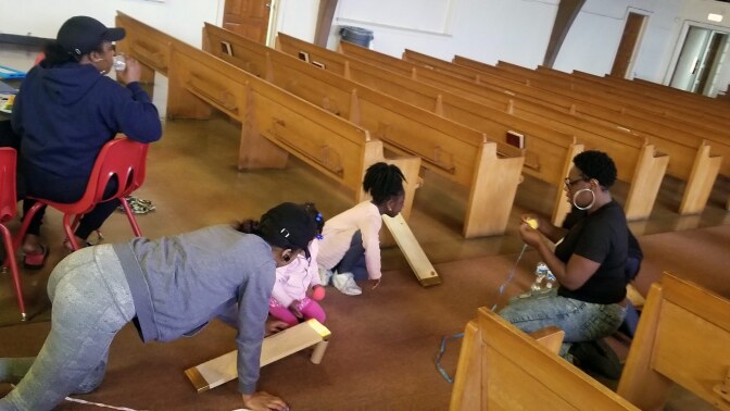 A small ramp on a carpet made out of a wood slat and propped up with two small water bottles