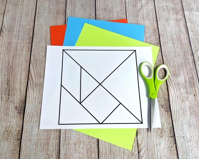 A template for a tangram is laid out on a table alongside some scissors and colorful paper.