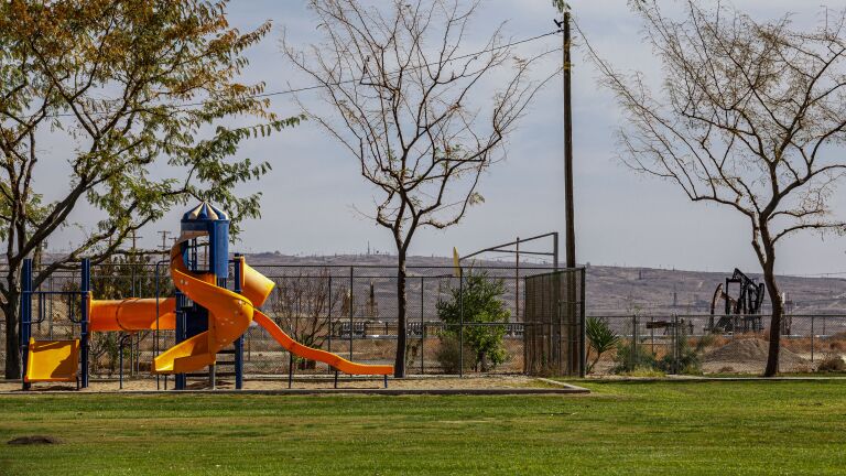 A colorful playground structure appears on the left with oil pumpjacks on the right and barren hills in the distance