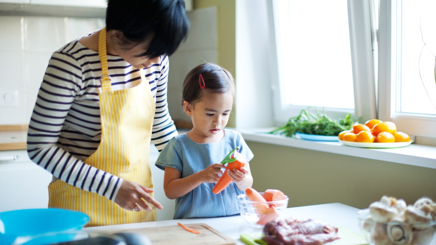 Mother working with small child to teach her how to use a vegetable peeler. cooking