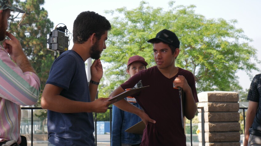 Luke and Ethan Montgomery look at one another on set, one holding a clipboard and scratching his chin. 