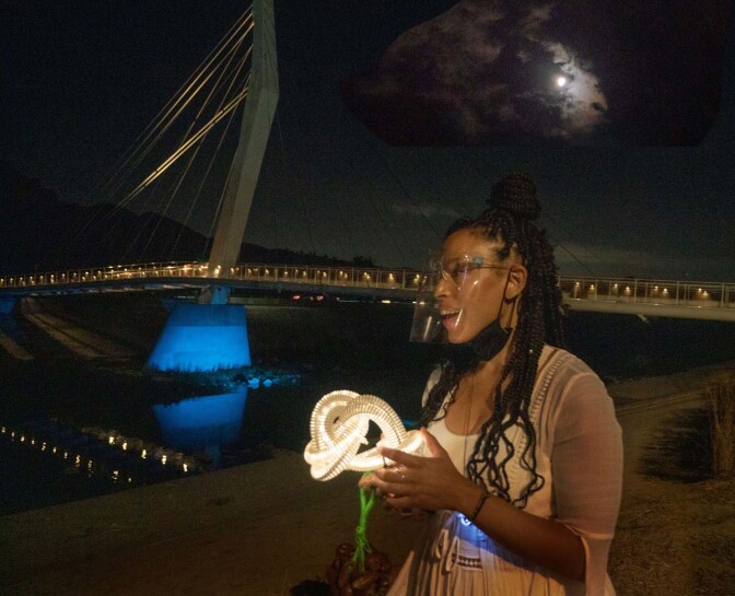 A perfomer wearing a face mask by the North Atwater Multi-modal Bridge. The performance is part of at "Firefly Nights," an in-person COVID-safe experience that falls within the "Rio Reveals" series.
