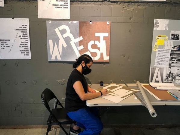 A woman with blue pants works on stencils at a desk.