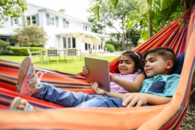 Young Hispanic siblings using digital tablet in hammock