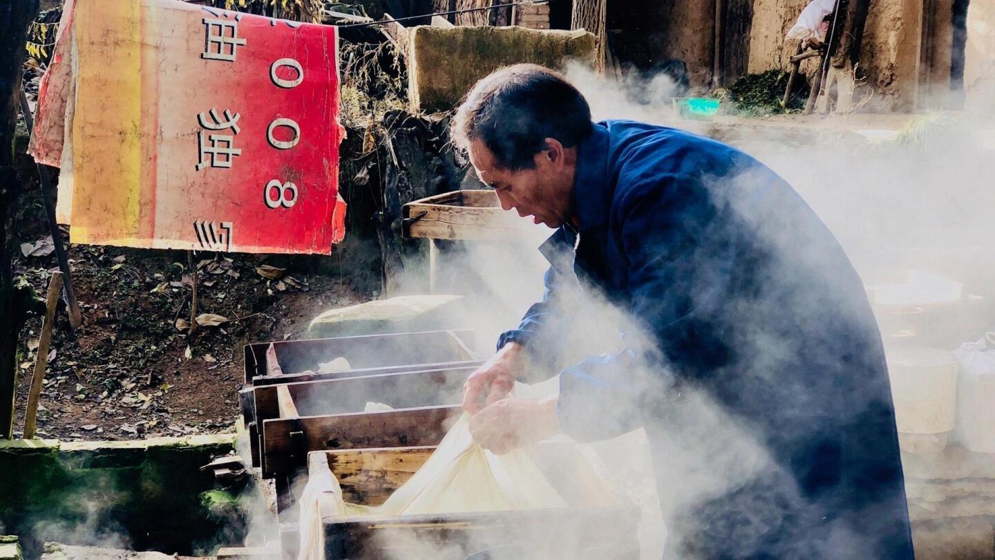 A man pulls on a sheet-like substance while engulfed in smoke. | "Voices from the Frontline: China's War on Poverty"