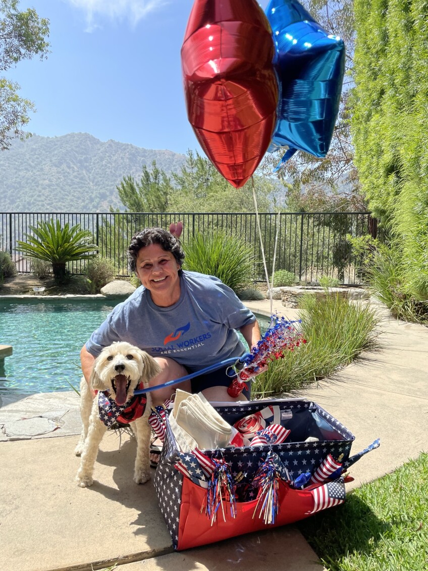 Person poses with their dog beside a pool and next to a basket of July 4th memorabilia.