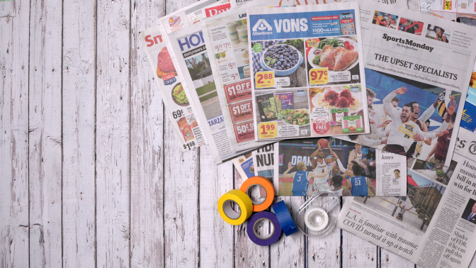 Colorful rolls of tape are laid out on a table alongside sheets of newspaper.