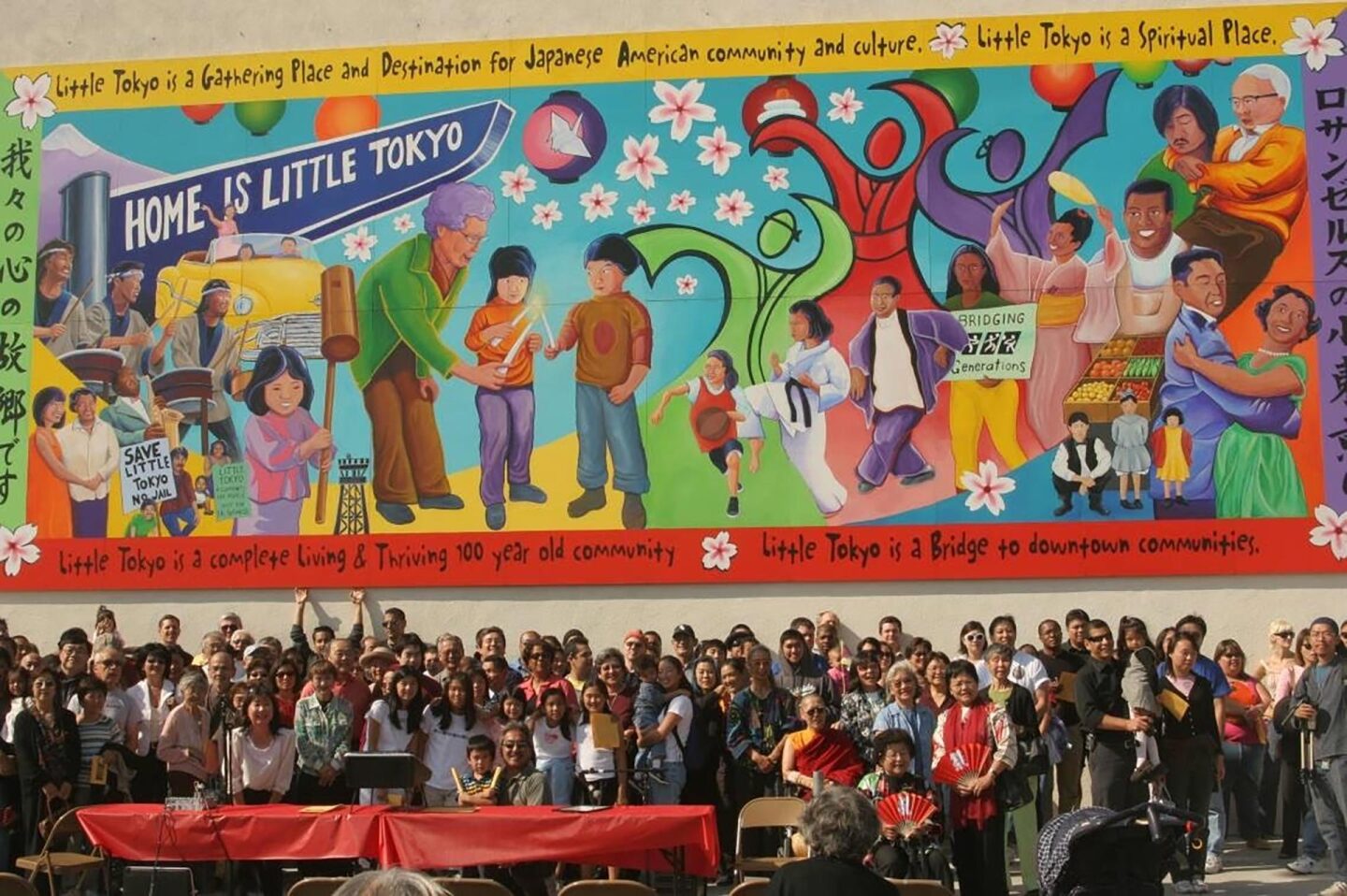 Dozens of people stand in front of a colorful mural depicting Japanese American history