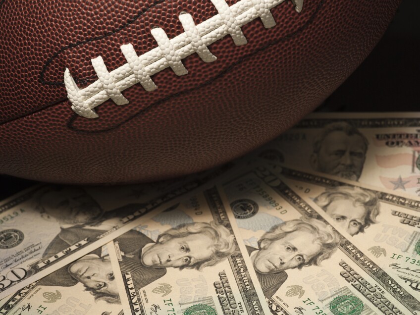 An American football rests on a pile of U.S. currency, including $20 and $50 bills.