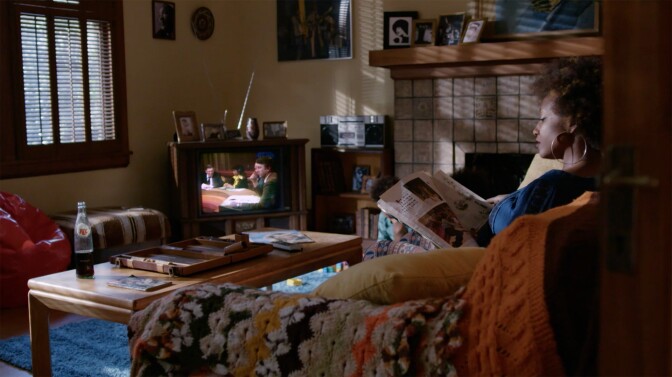 An African American woman sits in front of a television screen as they debate Proposition 13 | Still from "The First Angry Man"