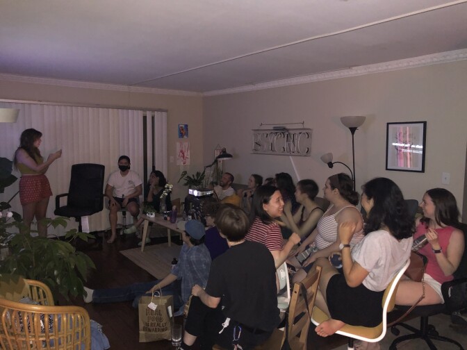 A large group of people sit in a living room. They're all facing a television out of frame.