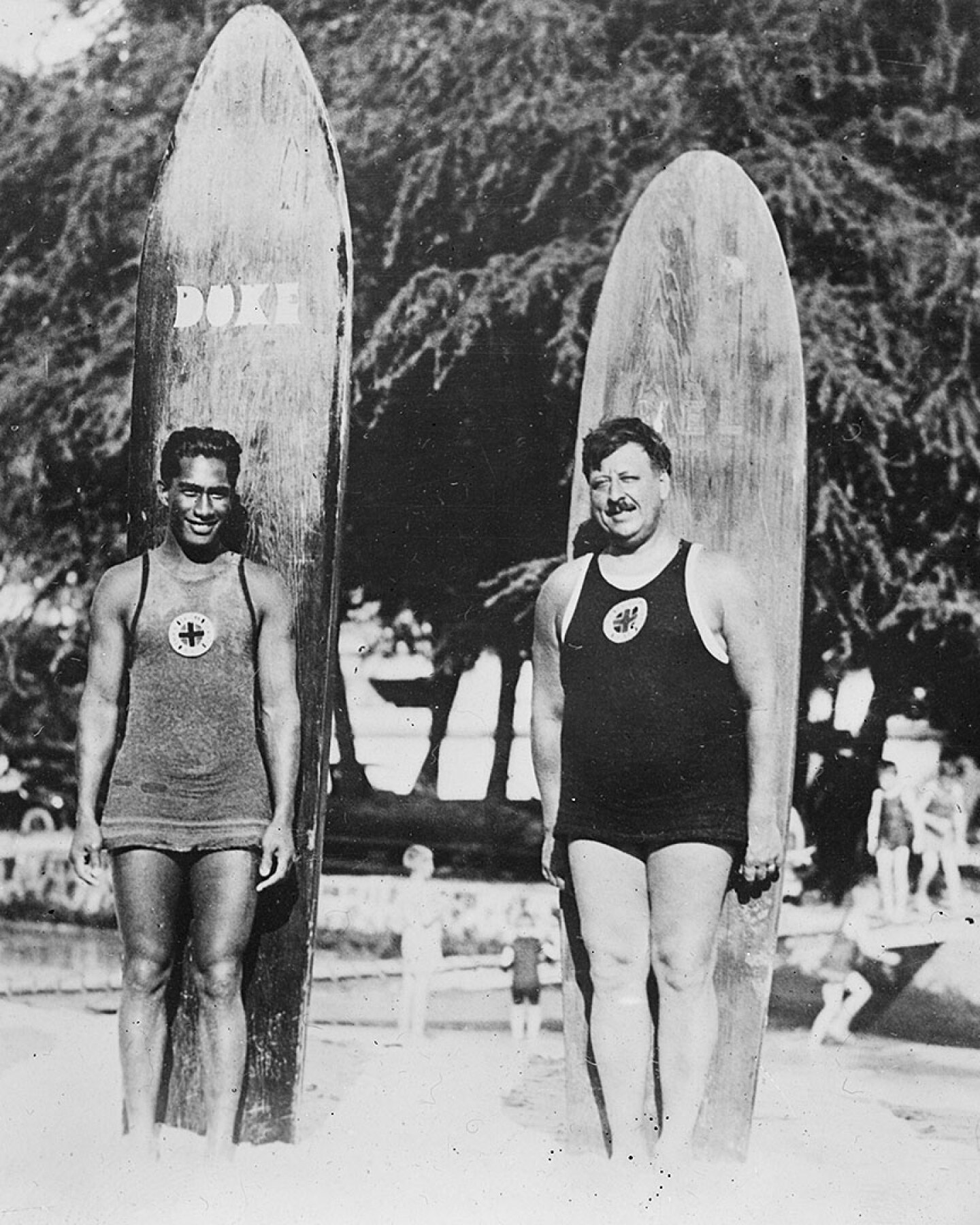 Four surfers stand in front of their boards- black and white