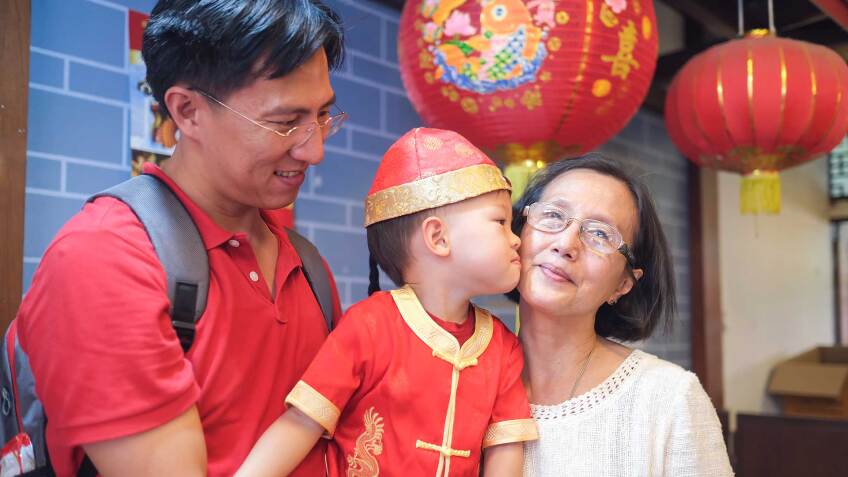 A father holding a t odder who kisses grandma as they celebrate Lunar New Year. | iStock