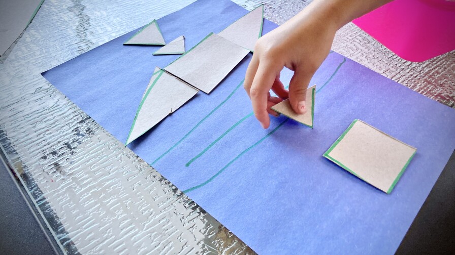 A child plays with a tangram made out of a cereal box.