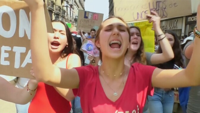Young people hold up signs at a climate protest. | Still from "The Youth Climate Movement Around the World" episode of "Earth Focus"