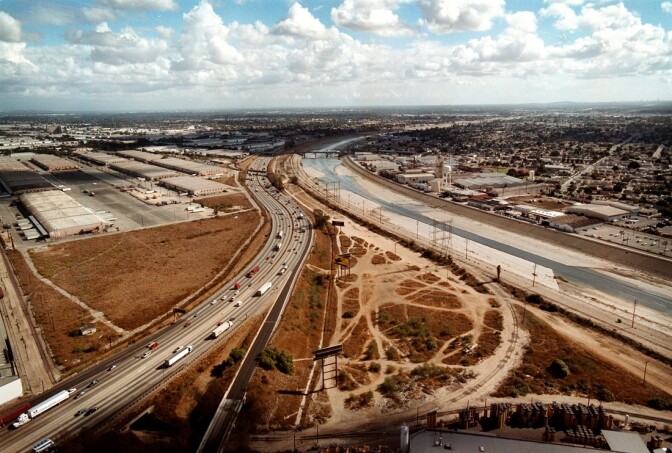 The cement-confined Los Angeles River, right, slides past open industrial lots in Los Angeles, CA