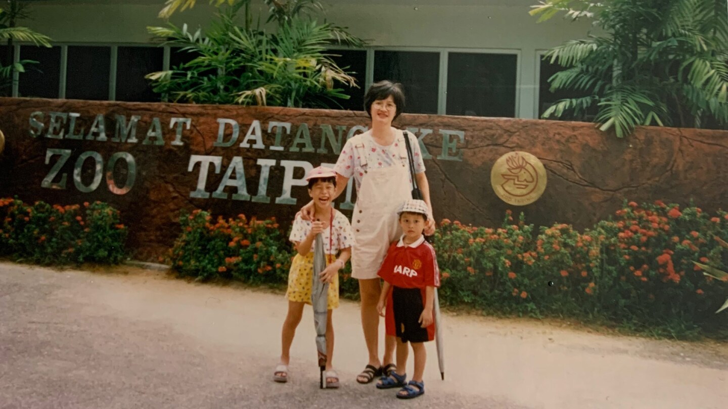 A woman stands in front of a zoo with two children
